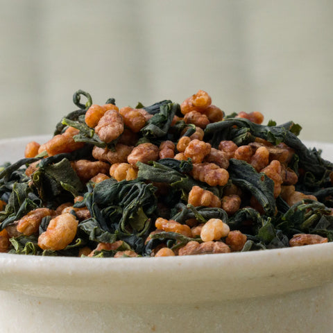 Genmaicha of green tea leaves mixed with roasted puffed brown rice piled in a ceramic bowl, side view.