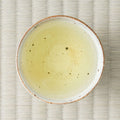 Pale yellow-green Kumamoto kamairi genmaicha brewed in a ceramic cup, viewed from above on tatami.