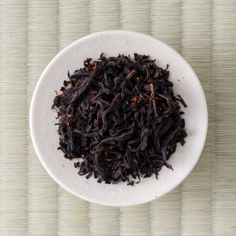 Dark twisted Kumamoto Koushun wakoucha leaves in a cream dish, viewed from above.