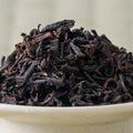 Close-up of Kumamoto Zairai wakoucha leaf, dark twisted strands with reddish stems, mounded in a pale bowl