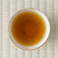 Kumamoto Zairai wakoucha brewed to a deep amber liquor in a speckled white cup, shot from overhead on tatami