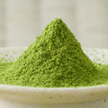 Bright green Miyama matcha powder heaped in a tall cone in a cream bowl, close side view.
