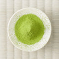 Bright green Miyama matcha powder mounded in a white dish, viewed from above on a tatami mat.