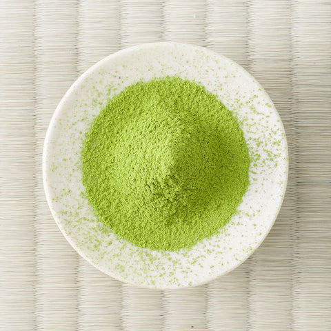 Bright green Miyama matcha powder mounded in a white dish, viewed from above on a tatami mat.