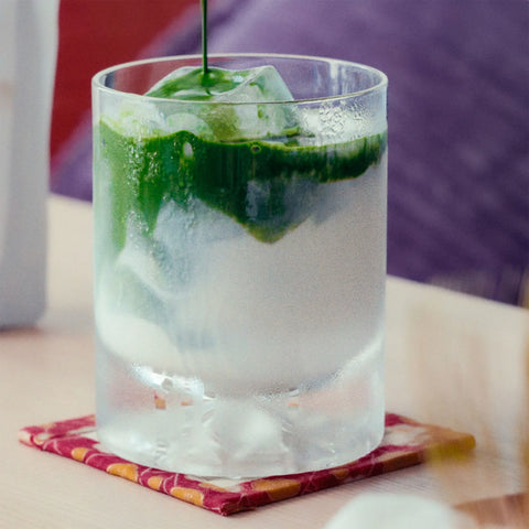 Iced matcha latte in a tall glass, a stream of dark green matcha pouring over ice and milk.