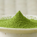 Bright green Moegi matcha powder heaped in a sharp cone in a cream ceramic bowl, side view.