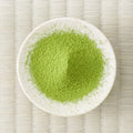 Yellow-green Moegi matcha powder mounded in a white dish, viewed from above on a tatami mat.