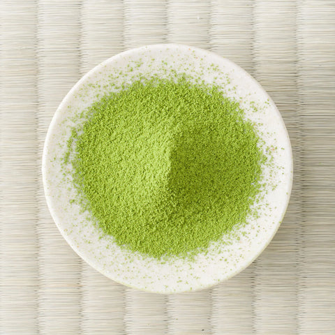 Yellow-green Moegi matcha powder mounded in a white dish, viewed from above on a tatami mat.