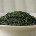 Fine dark-green Nukata Shunmei fukamushicha leaves piled in a ceramic bowl, side view.