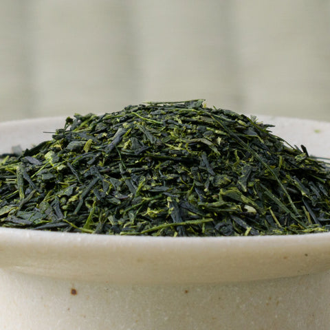 Fine dark-green Nukata Shunmei fukamushicha leaves piled in a ceramic bowl, side view.