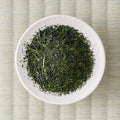 Fine dark-green Nukata Shunmei deep-steamed sencha leaves in a cream dish, viewed from above.
