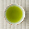 Vivid cloudy-green Nukata Shunmei fukamushicha (deep-steamed sencha) brewed in a ceramic cup, viewed from above on tatami.