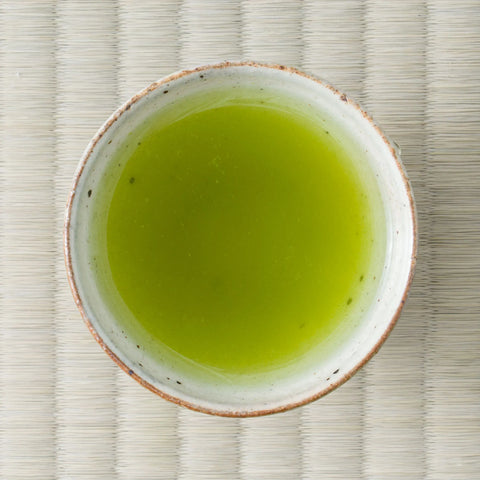 Vivid cloudy-green Nukata Shunmei fukamushicha (deep-steamed sencha) brewed in a ceramic cup, viewed from above on tatami.