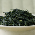 Dry deep-green Ryokuin sencha leaves mounded in a ceramic bowl, side view.