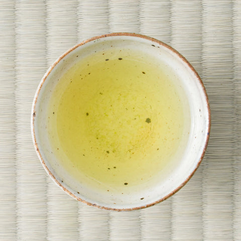 Yellow-green Ryokuin sencha brewed in a ceramic cup, viewed from above on a tatami mat.