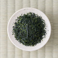 Deep green needle-shaped Satsuma Saemidori sencha leaves in a cream dish, viewed from above.