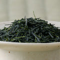 Deep green needle-shaped Satsuma Saemidori sencha leaves piled in a ceramic bowl, side view.