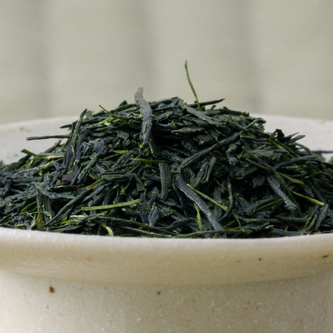Deep green needle-shaped Satsuma Saemidori sencha leaves piled in a ceramic bowl, side view.