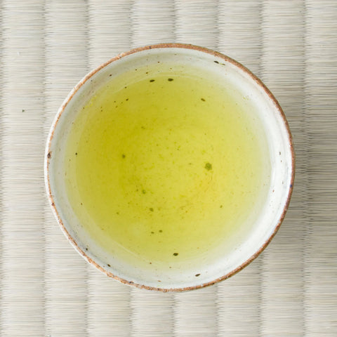 Bright yellow-green Satsuma Saemidori sencha brewed in a ceramic cup, viewed from above on tatami.