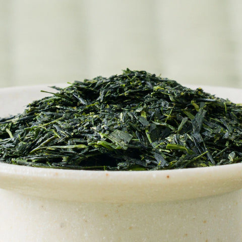 Dry deep-green fine Senryu fukamushicha leaves mounded in a ceramic bowl, side view.