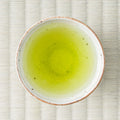 Vivid green Senryu fukamushicha brewed in a ceramic cup, viewed from above on a tatami mat.