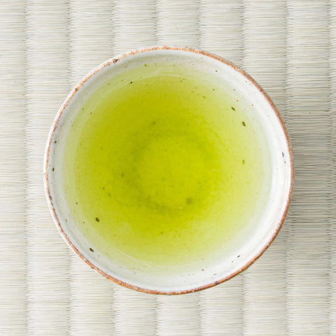 Vivid green Senryu fukamushicha brewed in a ceramic cup, viewed from above on a tatami mat.