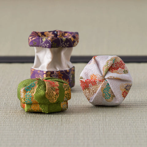 Three silk kogo on tatami with the purple one opened to reveal the white porcelain container inside, green and blush kogo closed in front