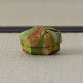 Silk kogo wrapped in moss-green brocade with gold and coral floral motifs, side view on a tatami mat