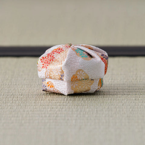 Blush and gold floral brocade silk kogo photographed from the side on tatami, its lid resting slightly askew on the body