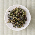 Green-brown twisted Takachiho Benifuki oolong leaves in a cream dish, viewed from above.