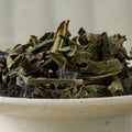 Dry green-brown twisted Takachiho Benifuki oolong leaves piled in a ceramic bowl, side view.
