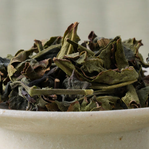 Dry green-brown twisted Takachiho Benifuki oolong leaves piled in a ceramic bowl, side view.