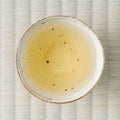 Pale golden Takachiho Benifuki oolong brewed in a ceramic cup, viewed from above on tatami.