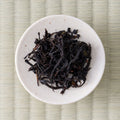 Dark twisted Takachiho Minamisayaka wakoucha loose-leaf black tea in a small cream dish, viewed from above.