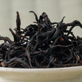 Dry twisted dark reddish-brown Takachiho Minamisayaka wakoucha leaves piled in a ceramic bowl, side view.
