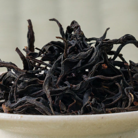 Dry twisted dark reddish-brown Takachiho Minamisayaka wakoucha leaves piled in a ceramic bowl, side view.
