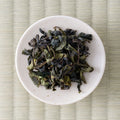 Green-brown twisted Takachiho oolong leaves in a cream dish, viewed from above.