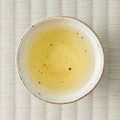 Pale golden-yellow Takachiho oolong brewed in a ceramic cup, viewed from above on tatami.