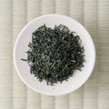 Dark green curled Takachiho Tokujo kamairicha leaves in a cream dish, viewed from above.