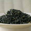 Dark green curled Takachiho Tokujo kamairicha leaves piled in a ceramic bowl, side view.