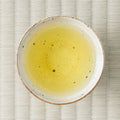 Pale yellow-green Takachiho Tokujo kamairicha (pan-fired green tea) brewed in a ceramic cup, viewed from above on tatami.