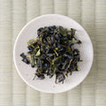 Dark green twisted Takachiho Unkai oolong leaves in a cream dish, viewed from above.