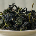 Dry dark green Takachiho Unkai oolong leaves piled in a ceramic bowl, side view.