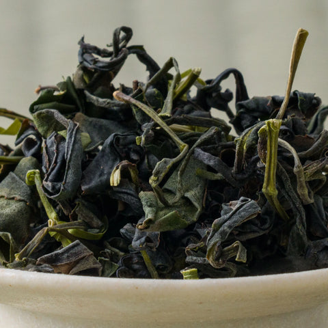 Dry dark green Takachiho Unkai oolong leaves piled in a ceramic bowl, side view.