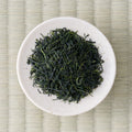 Dry deep-green needle-shaped Uji temomi gyokuro leaves in a cream dish, viewed from above.