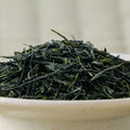 Dry deep-green needle-shaped temomi gyokuro leaves piled in a ceramic bowl, side view.