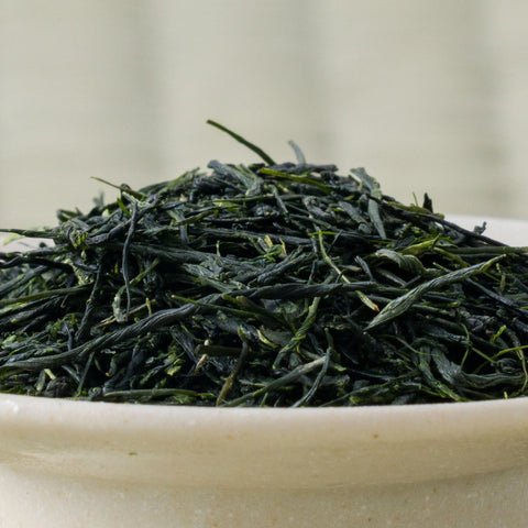 Dry deep-green needle-shaped temomi gyokuro leaves piled in a ceramic bowl, side view.