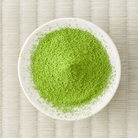 Vivid green Tōzan matcha powder mounded in a white dish on a tatami mat, overhead view.