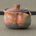 Reddish shino-glazed lidded houhin, close side view on a tatami mat.