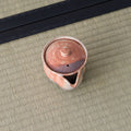 Overhead view of a reddish shino-glazed houhin showing its lid and pouring spout, on a tatami mat.